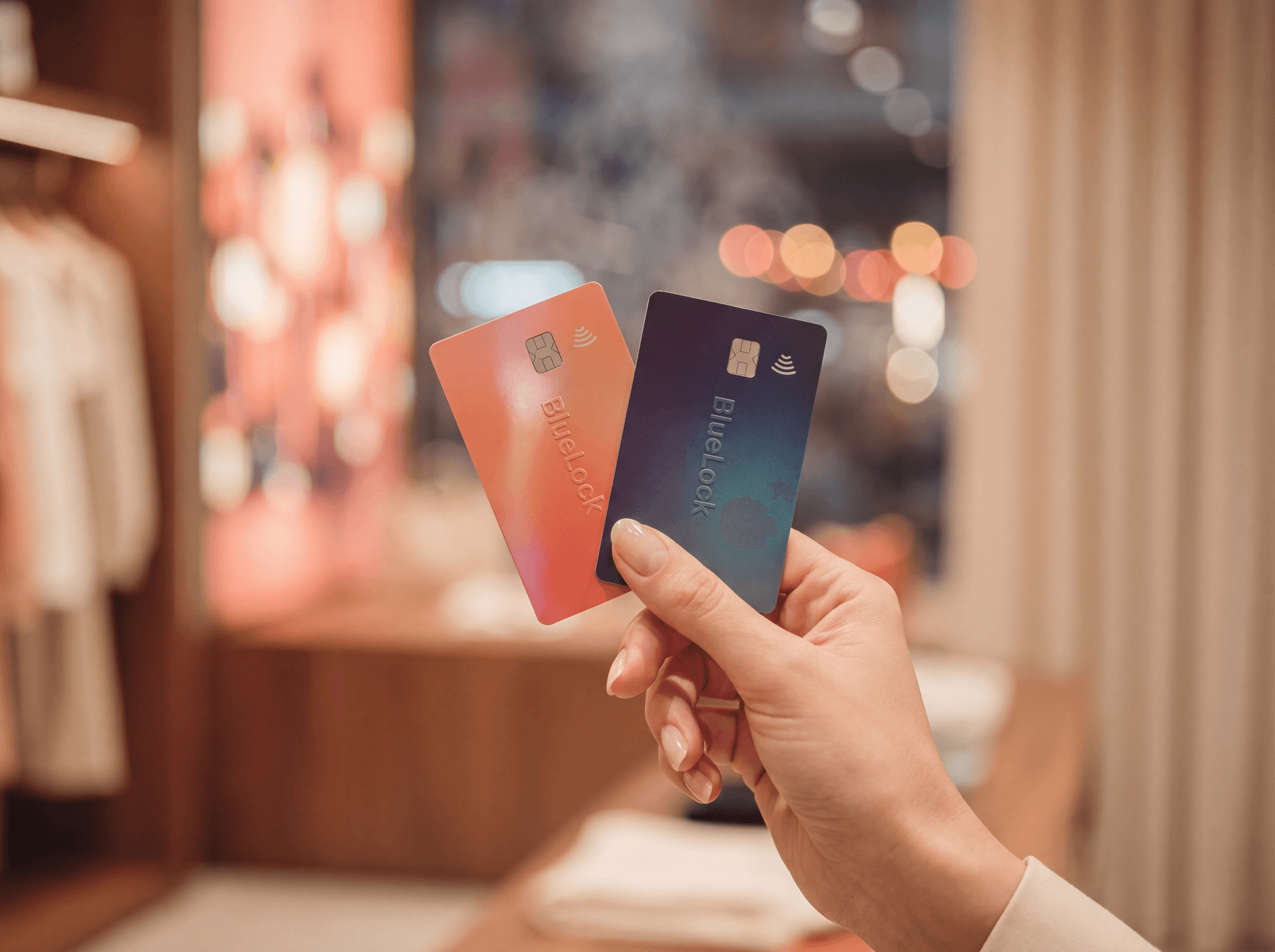 Mão segurando dois cartões BlueLock — Visa coral e Mastercard indigo